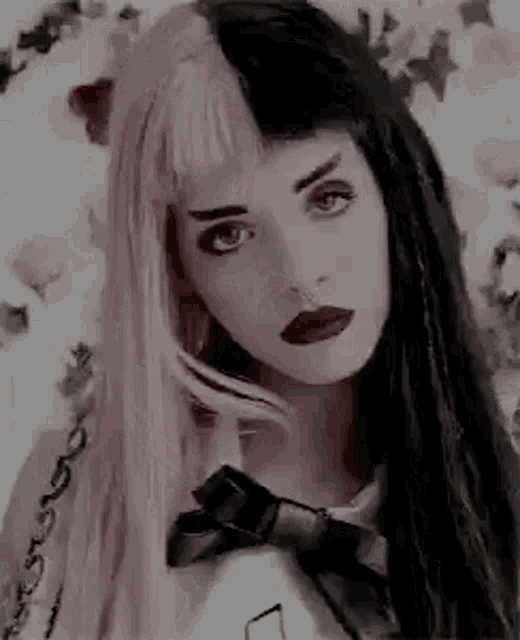 a woman with pink and black hair and a nose ring is wearing a black and white shirt and a bow tie .