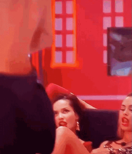 a couple of women are sitting on a couch in a room with a red wall .