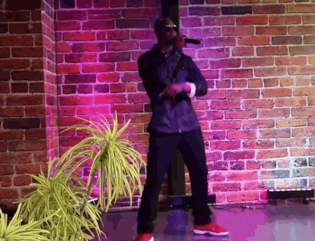 a man stands in front of a brick wall holding a microphone