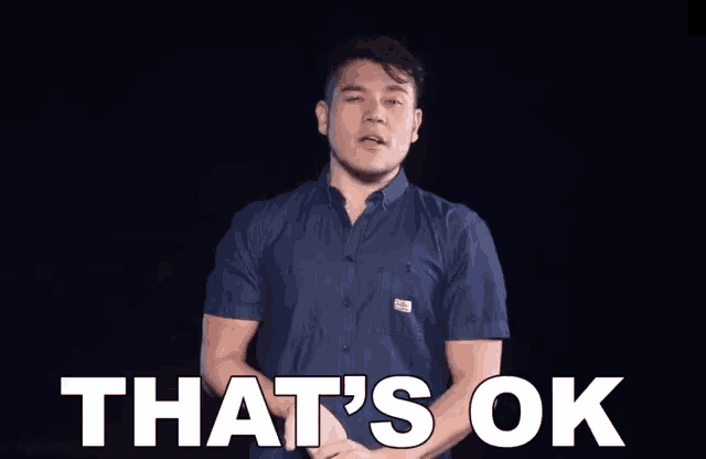 a man in a blue shirt is saying that 's ok with his arms outstretched