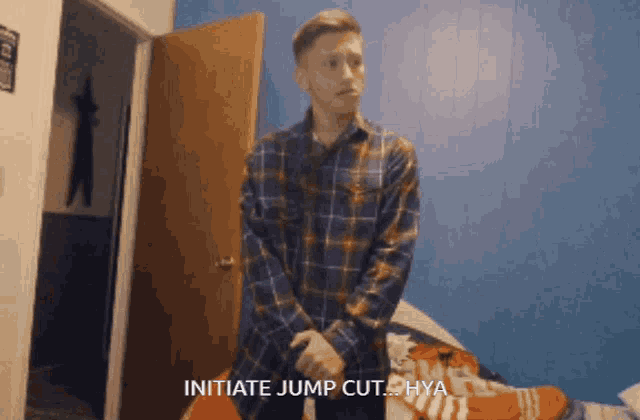 a man in a plaid shirt is standing in a bedroom and says initiate jump cut hya