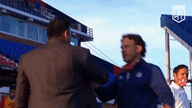 a man in a suit is shaking hands with another man in front of a stadium .