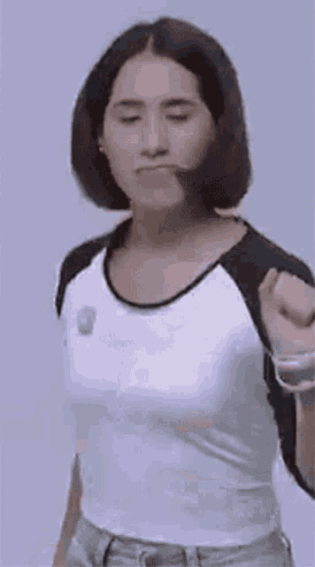 a woman with short hair is wearing a white shirt and jeans and is making a funny face .