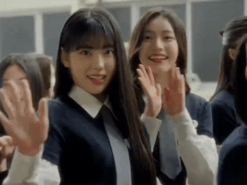 a group of young girls are standing in a classroom waving their hands .