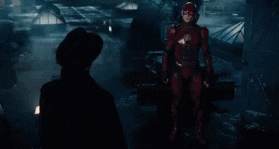 a man in a superhero costume is standing next to a woman in a black hat in a dark room .