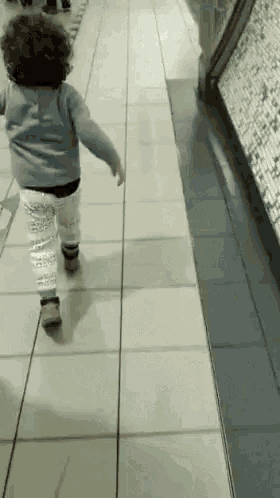 a little girl with curly hair is walking on a tiled floor