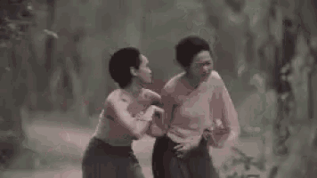 two women are standing next to each other in a dark forest .