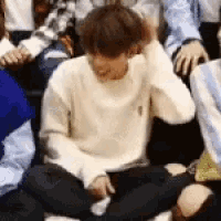 a man in a white sweater is sitting on the floor with his legs crossed and holding his hair .
