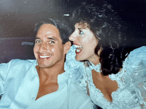 a man and woman are posing for a picture and the woman is wearing a wedding dress