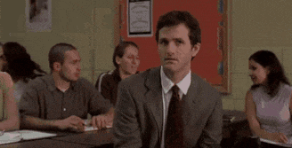 a man in a suit and tie is sitting at a desk in a classroom .