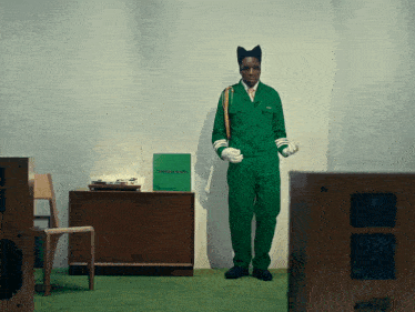 a man in a green jumpsuit is standing in front of a record player with a green record case that says groove hound