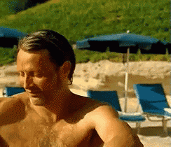 a shirtless man sitting on a beach with blue chairs and umbrellas