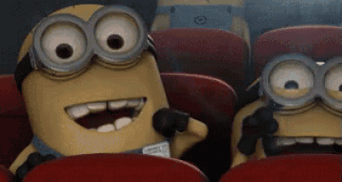a group of minions are sitting in red seats in a movie theater .
