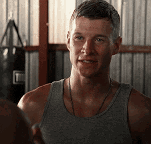 a man in a grey tank top is smiling in front of a boxing bag