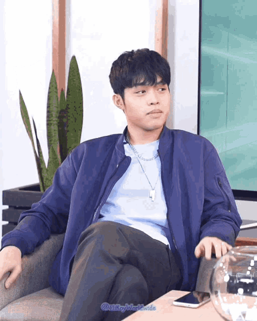 a young man in a blue jacket sits in a chair