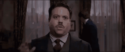 a man in a suit and tie is standing in a room with his hand out .