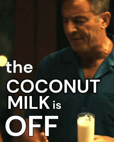 a man in a blue shirt is holding a glass of milk with the words the coconut behind him