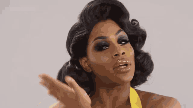 a woman in a yellow dress and wig is making a gesture with her hand .