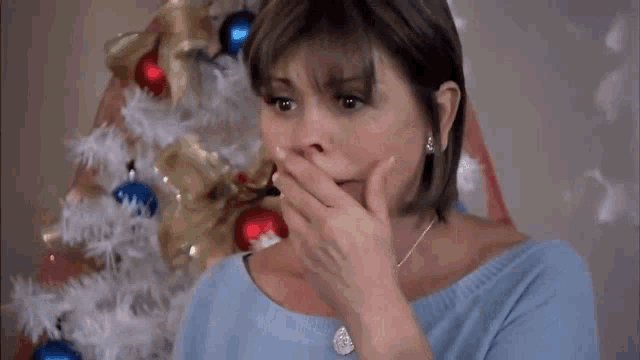 a woman covering her mouth in front of a christmas tree