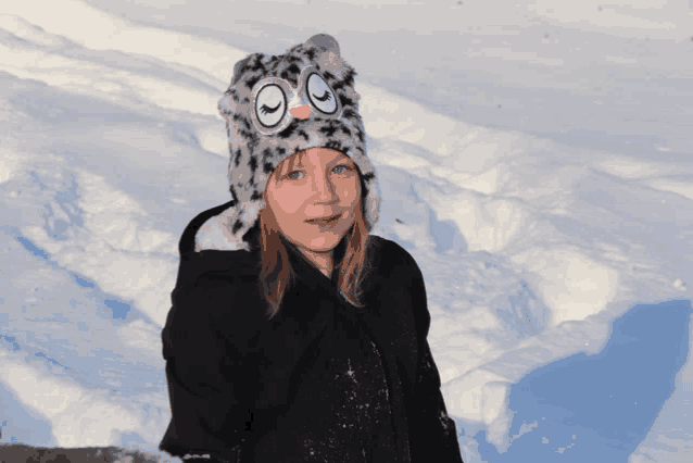 a young girl wearing a leopard print hat stands in a snowy field
