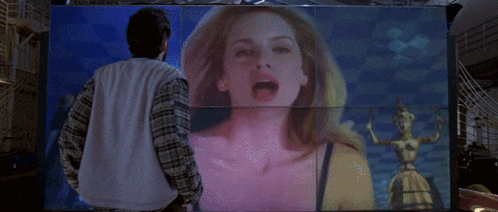 a man stands in front of a large screen that shows a woman