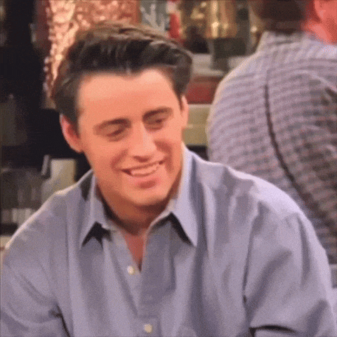 a man in a blue shirt is smiling while sitting in a bar .