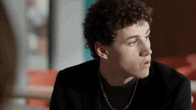 a young man with curly hair is wearing a black shirt and a necklace .