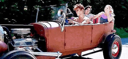 a group of people are riding in a red hot rod .