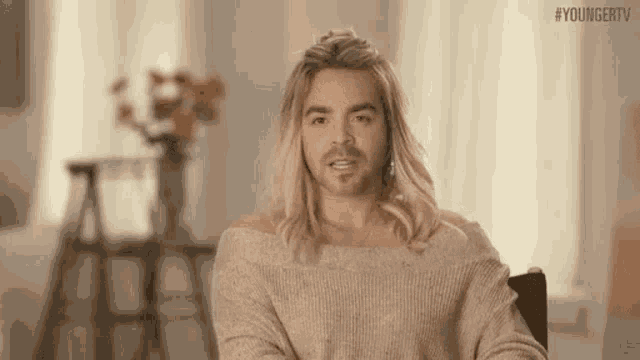 a man with long blonde hair and a beard is wearing a sweater and making a funny face .
