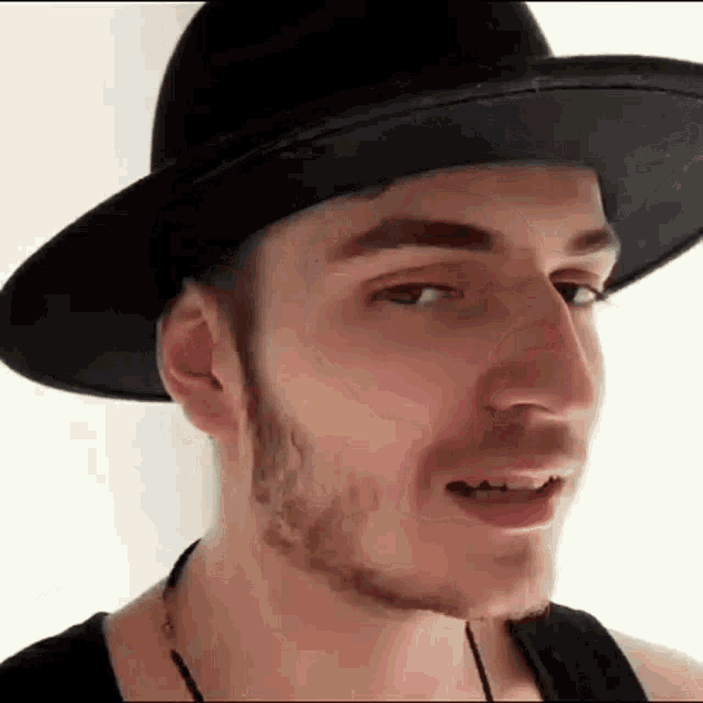 a young man with a beard wearing a black hat and a black tank top .