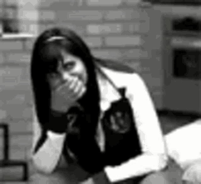 a black and white photo of a woman sitting on the floor covering her mouth with her hand .