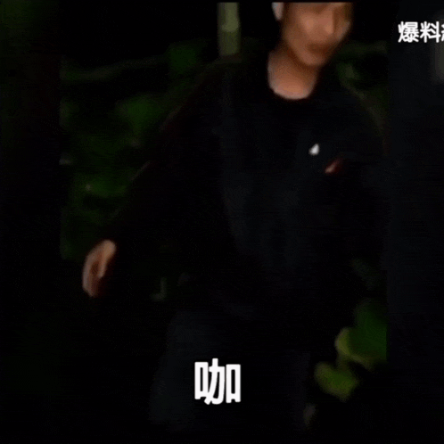 a man in a black shirt is standing in the dark with chinese writing on his chest