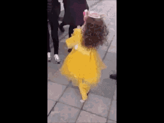 a dog wearing a yellow dress and pink sunglasses is being pulled by a person .