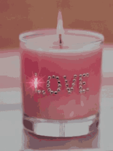 a pink candle in a glass with the word love on it