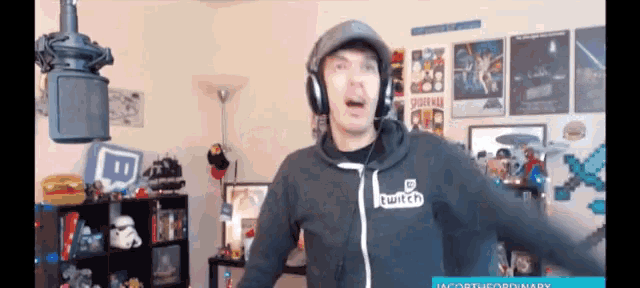 a man wearing headphones and a twitch hoodie stands in front of a microphone