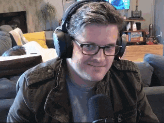 a man wearing headphones and glasses is sitting in front of a microphone and smiling .