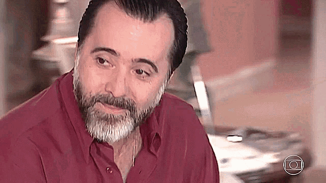a man with a beard wearing a red shirt is looking at the camera