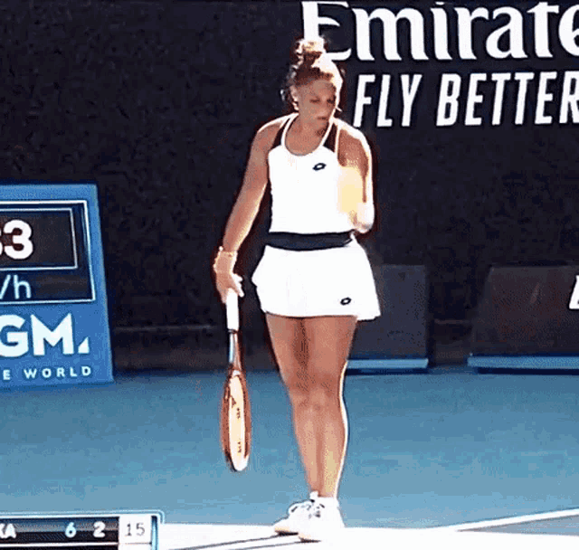 a woman is holding a tennis racquet in front of an emirates fly better banner