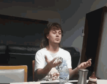 a young man sitting at a table with a bottle of water in front of him