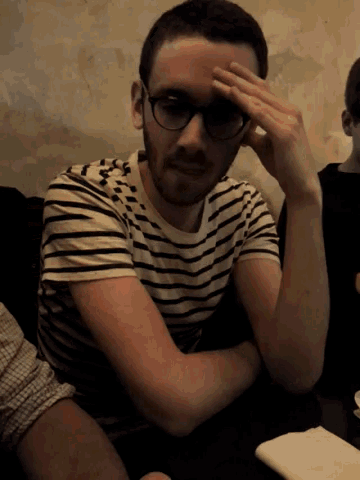 a man wearing glasses and a striped shirt holds his hand to his face