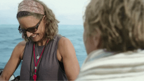 a woman wearing sunglasses and a headband smiles while talking to another woman
