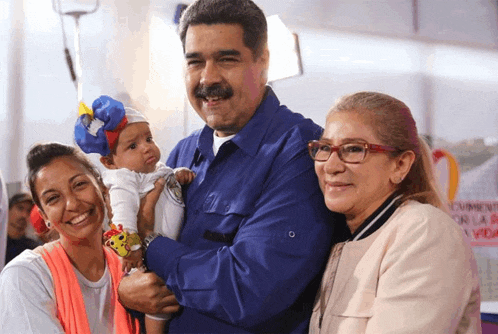 a man in a blue shirt holds a baby while two women smile