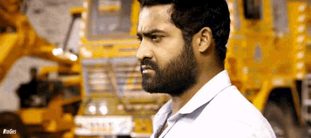 a man with a beard stands in front of a yellow truck with the word windows on the bottom