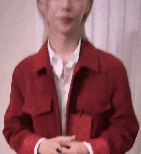 a man wearing a red jacket and a white shirt is standing with his hands folded .