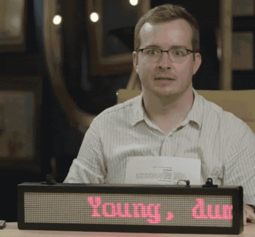 a man with glasses sits at a desk with a sign that says young