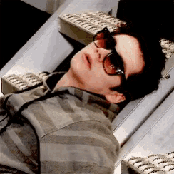 a man wearing sunglasses and a striped shirt is laying on a bed