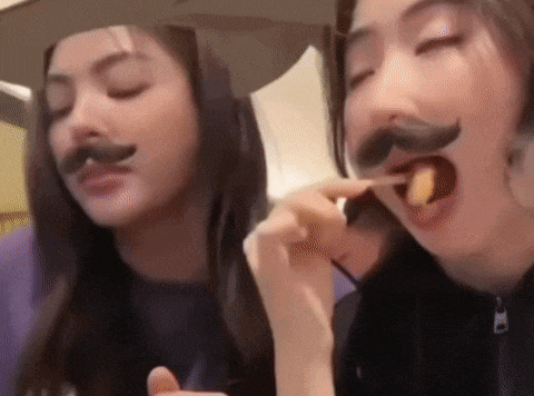 two women wearing fake mustaches are eating chips .