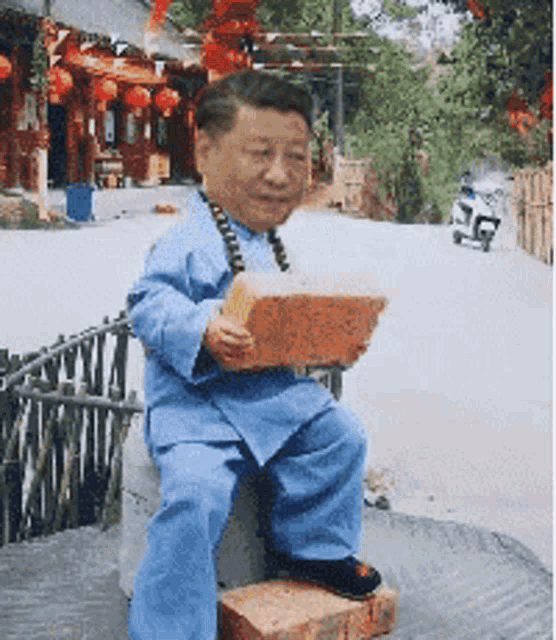 a man in a blue shirt is sitting on a brick holding a brick in his hand