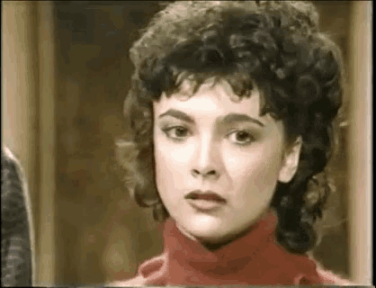 a woman with curly hair is wearing a red turtleneck sweater and making a funny face .