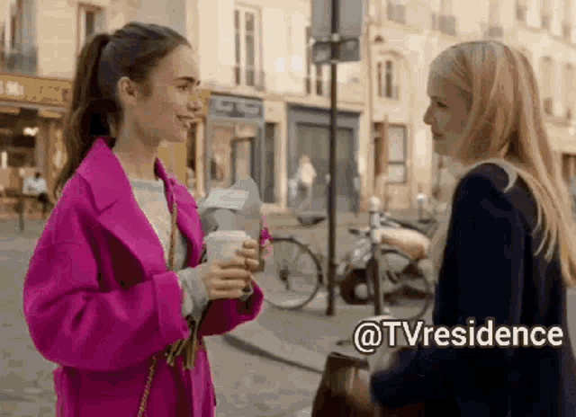 a woman in a pink coat is talking to another woman on a street .